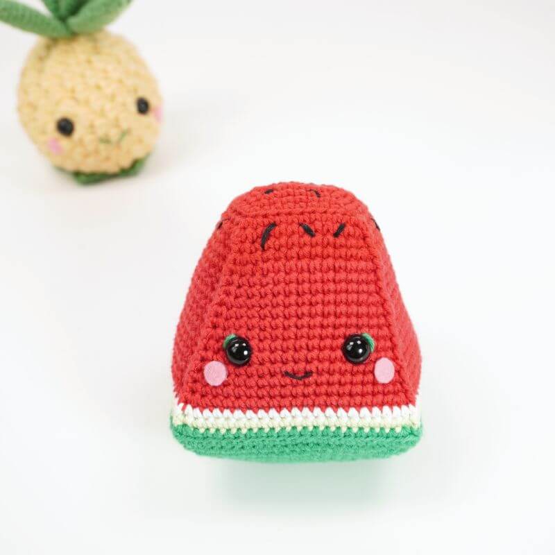 sandía de amigurumi con piña de crochet al fondo